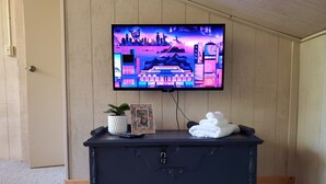 A room with a black dresser, a television on the wall, a potted plant, a framed photo, and folded towels. - Cozy 4bd - Ski Okemo, Killington, Magic & Bromley (Chester)