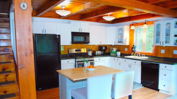 A kitchen with white cabinets, a black refrigerator, a microwave, a stove, and a sink. There are two white chairs at the island. - Cozy 4bd - Ski Okemo, Killington, Magic & Bromley (Chester)