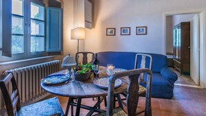 A dining area with a round table, chairs, a blue sofa, a radiator, and a window with blue shutters. - Beautiful apartment in villa for 6 people with pool, TV and patio (Poggibonsi)