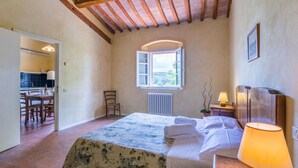 A bedroom with a bed, a window, a radiator, a chair, a table, and a lamp. - Beautiful apartment in villa for 6 people with pool, TV and patio (Poggibonsi)