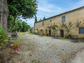 A courtyard with a gravel path, outdoor seating, and a building with multiple doors and windows. - Nice apartment in villa for 6 guests with pool, TV and patio (Poggibonsi)