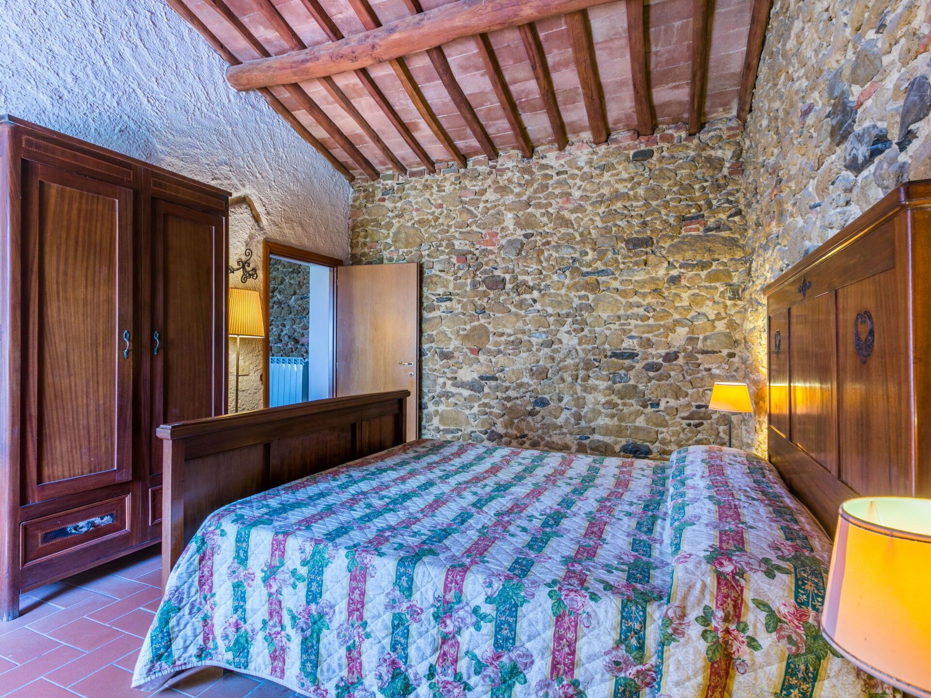 A bedroom with a stone wall, wooden bed frame, and a quilted bedspread.