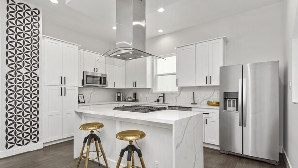 A modern kitchen with white cabinets, a stainless steel refrigerator, and two stools with gold seats. - The Hideaway EaDo with hot tub! (Houston)