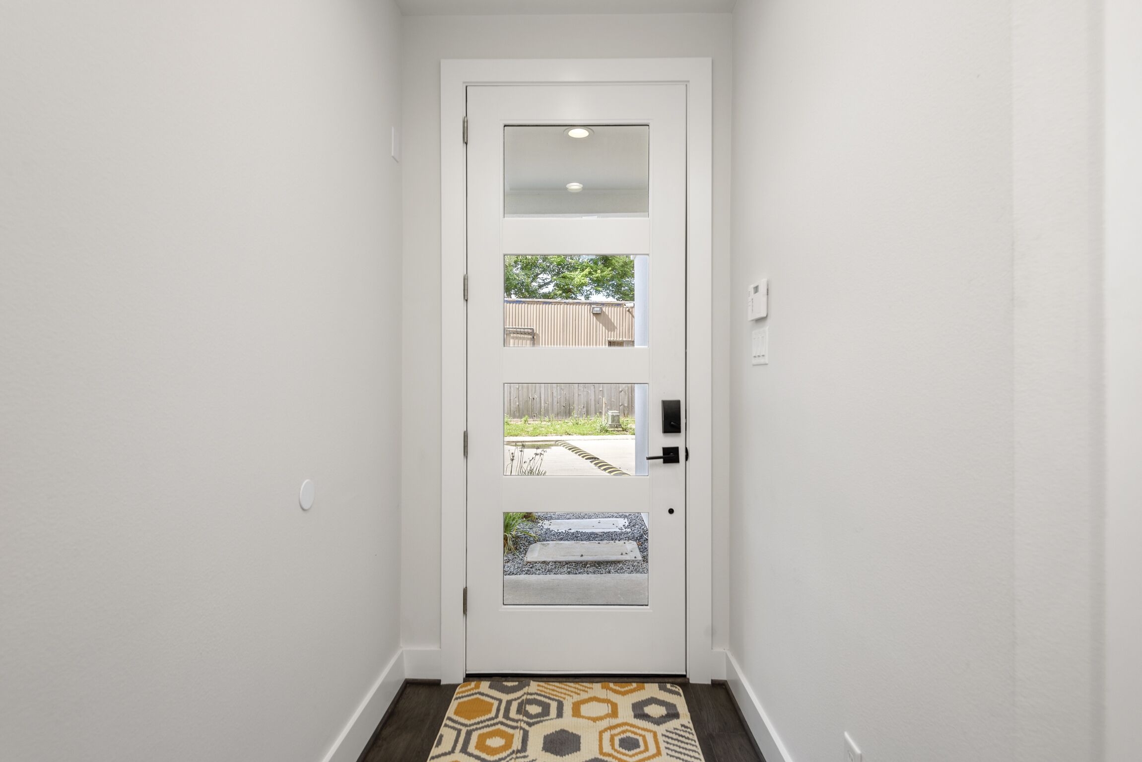 A white door with a glass panel and a small window, leading to an outdoor area with a concrete path and a wooden fence.