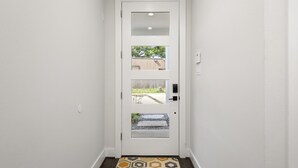 A white door with a glass panel and a small window, leading to an outdoor area with a concrete path and a wooden fence. - The Hideaway EaDo with hot tub! (Houston)