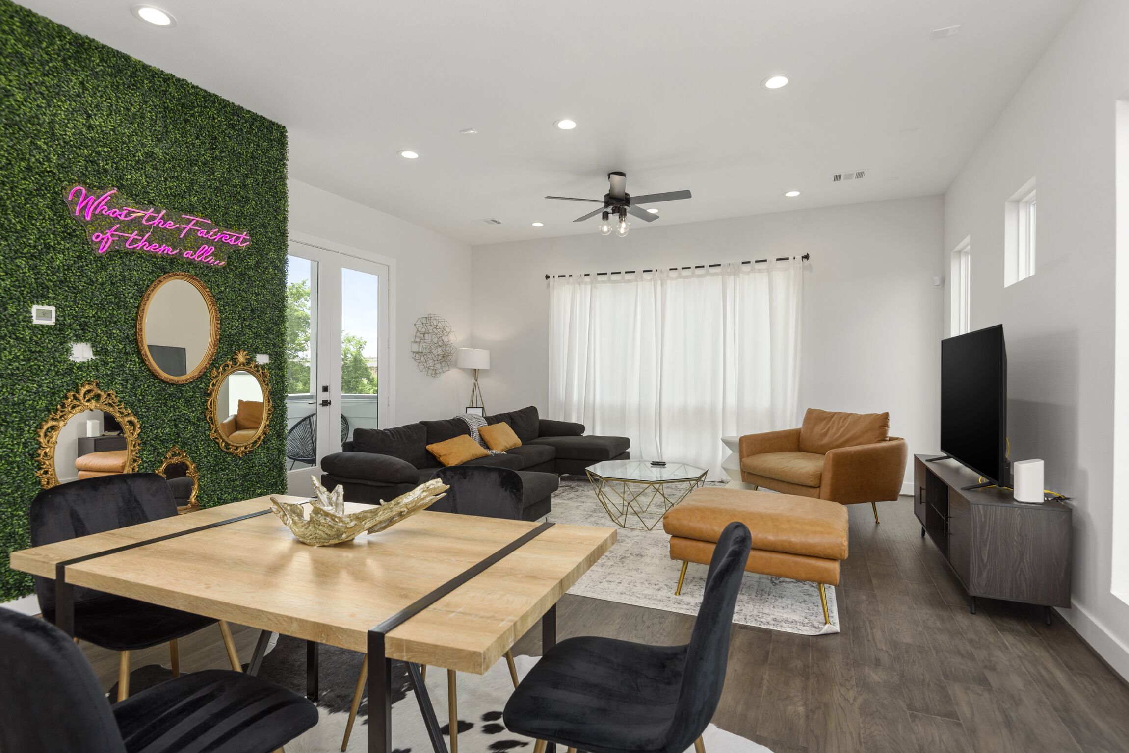 A modern living room with a dining area, a ceiling fan, and a TV.