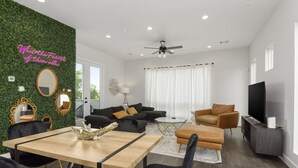 A modern living room with a dining area, a ceiling fan, and a TV. - The Hideaway EaDo with hot tub! (Houston)