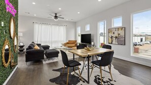 A modern living room with a sofa, chairs, a dining table, and a TV. - The Hideaway EaDo with hot tub! (Houston)