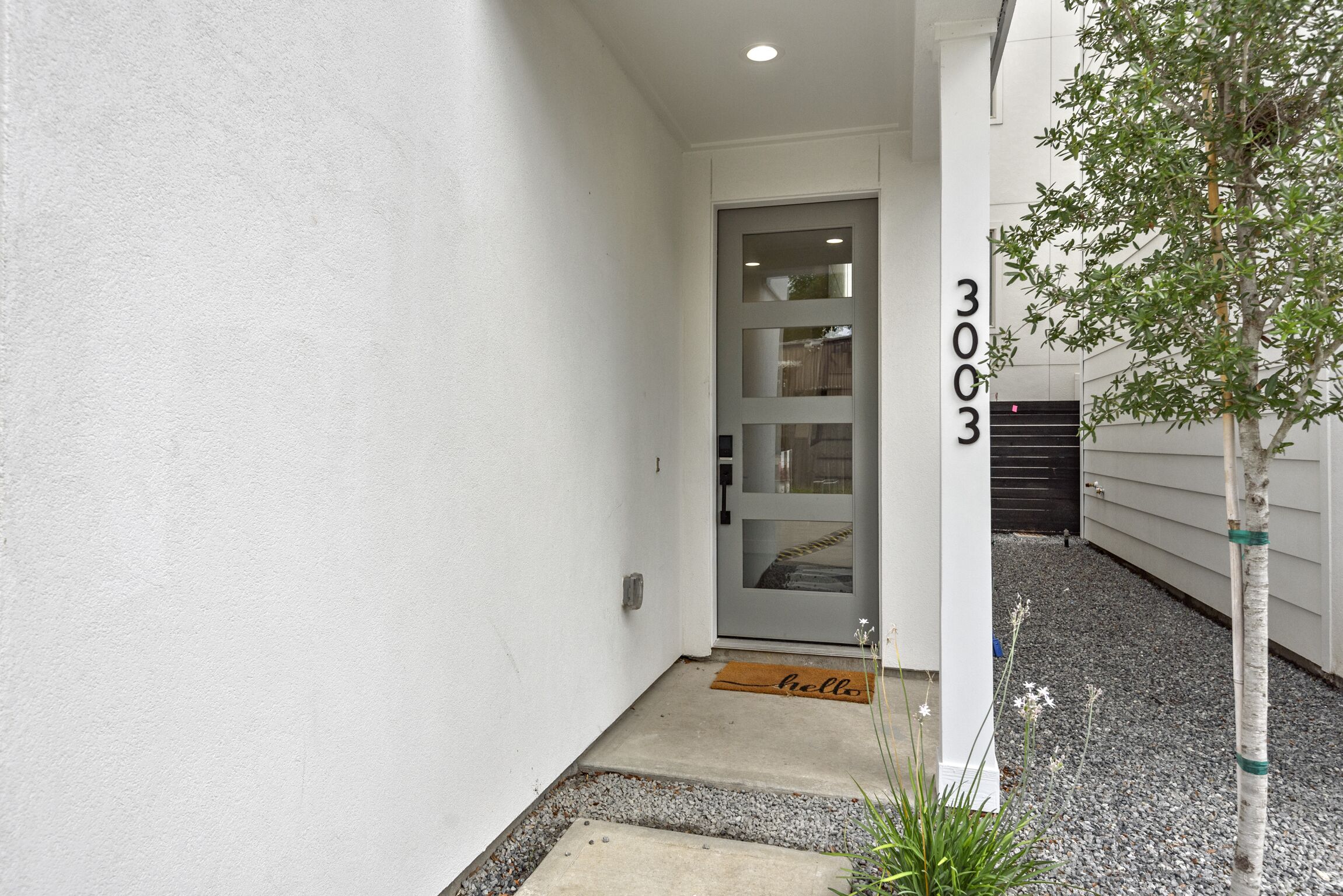 A white exterior wall with a door, a mailbox, and a small tree.