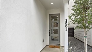 A modern entrance with a glass door, a doormat, and a small tree. - The Hideaway EaDo with hot tub! (Houston)