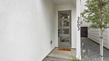 A white exterior wall with a door, a mailbox, and a small tree.