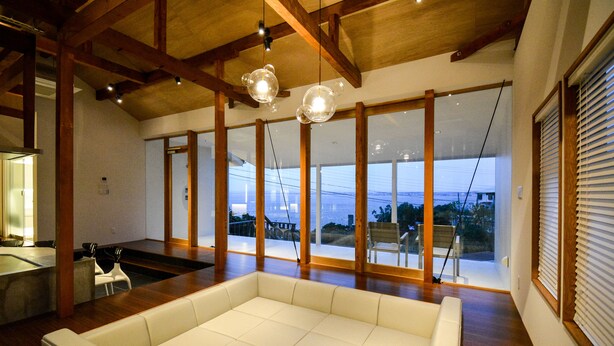A spacious living area with a large white sofa, wooden beams, and large windows offering a view of the outdoors. - Wellis Villa HANARE (Awaji)