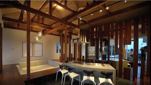 A modern kitchen with a central island, white bar stools, and wooden beams. - Wellis Villa HANARE (Awaji)