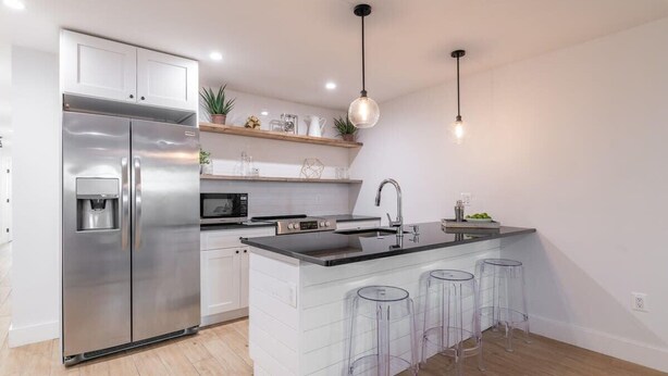 A modern kitchen with a stainless steel refrigerator, a microwave, a sink, and a bar area with stools. - Bloomingdale Beauty - Sleeps 4 in Style! (Washington)