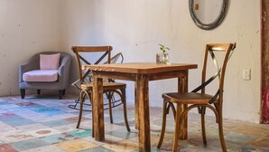 A dining area with a wooden table and four chairs, a grey armchair with a pink cushion, and a mirror on the wall. - Master Room on 5th, one block to the beach (Playa del Carmen)