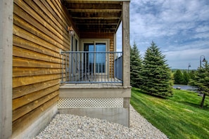 A wooden building with a balcony, gravel pathway, and a grassy area with trees.