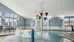 An indoor swimming pool with a water fountain, seating area, and large windows.
