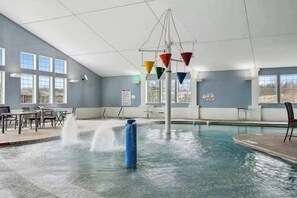 An indoor swimming pool with a water fountain, seating area, and large windows.