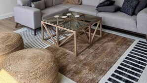 A modern living room with a sectional sofa, a glass coffee table, and a woven rug.