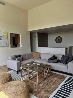 A modern living room with a sectional sofa, a glass coffee table, and a woven rug.