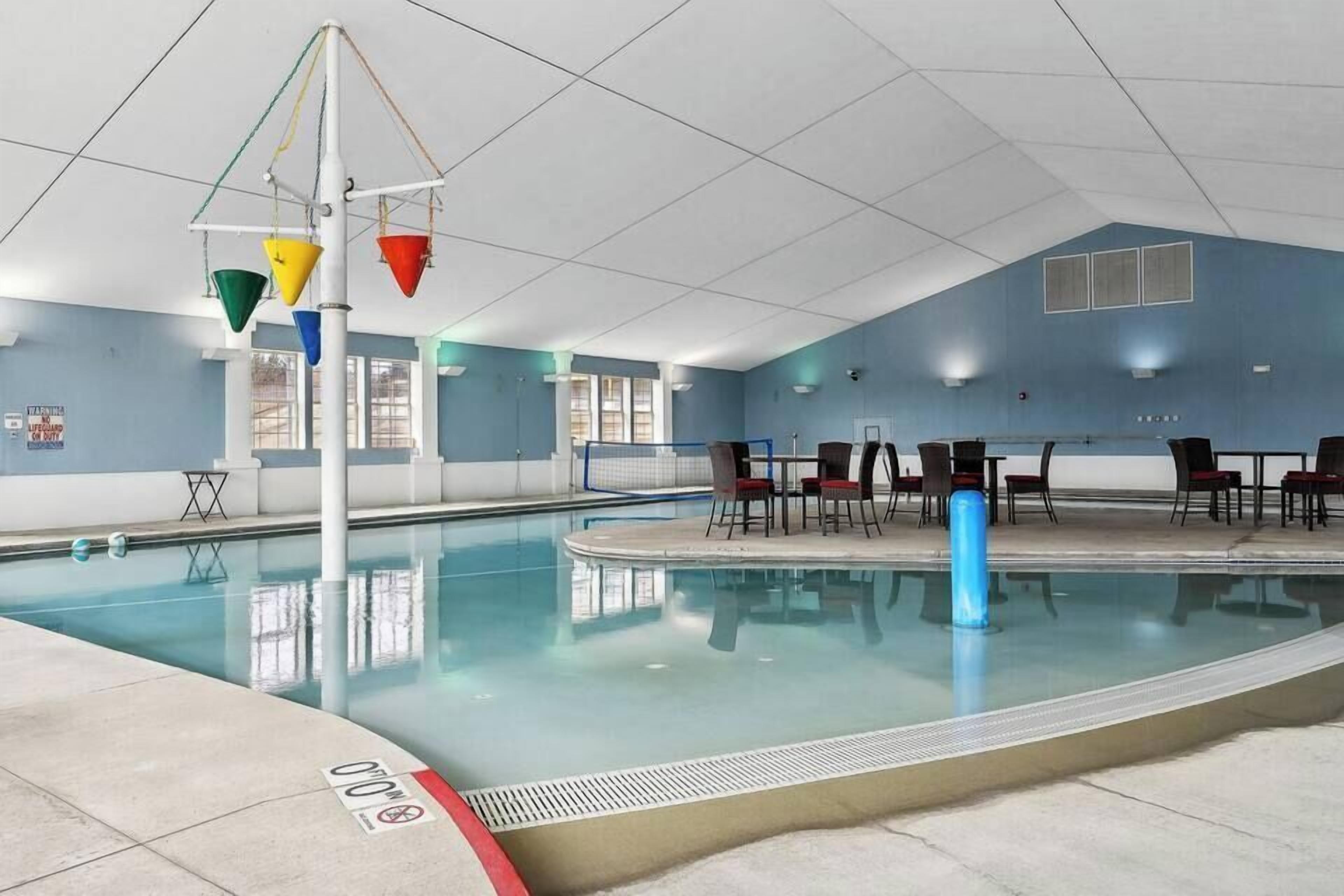 An indoor swimming pool with a diving board, chairs, and a blue wall.