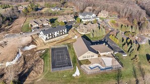 An aerial view of a residential area with houses, a tennis court, and a large building with a curved roof.