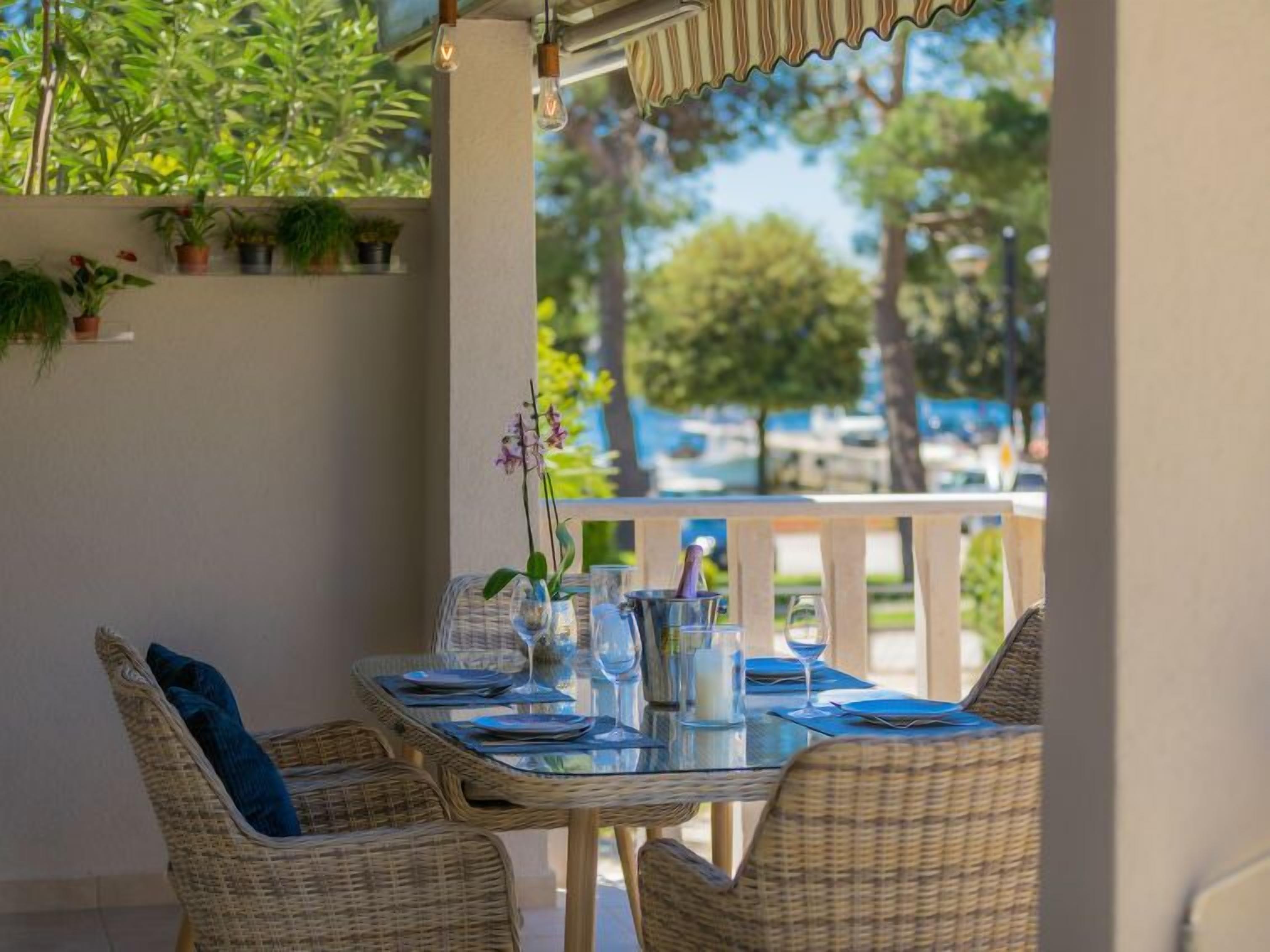 Un espace extérieur aménagé pour les repas, avec des chaises en osier et une table en verre pour deux personnes, offrant une vue sur une marina et ses bateaux.