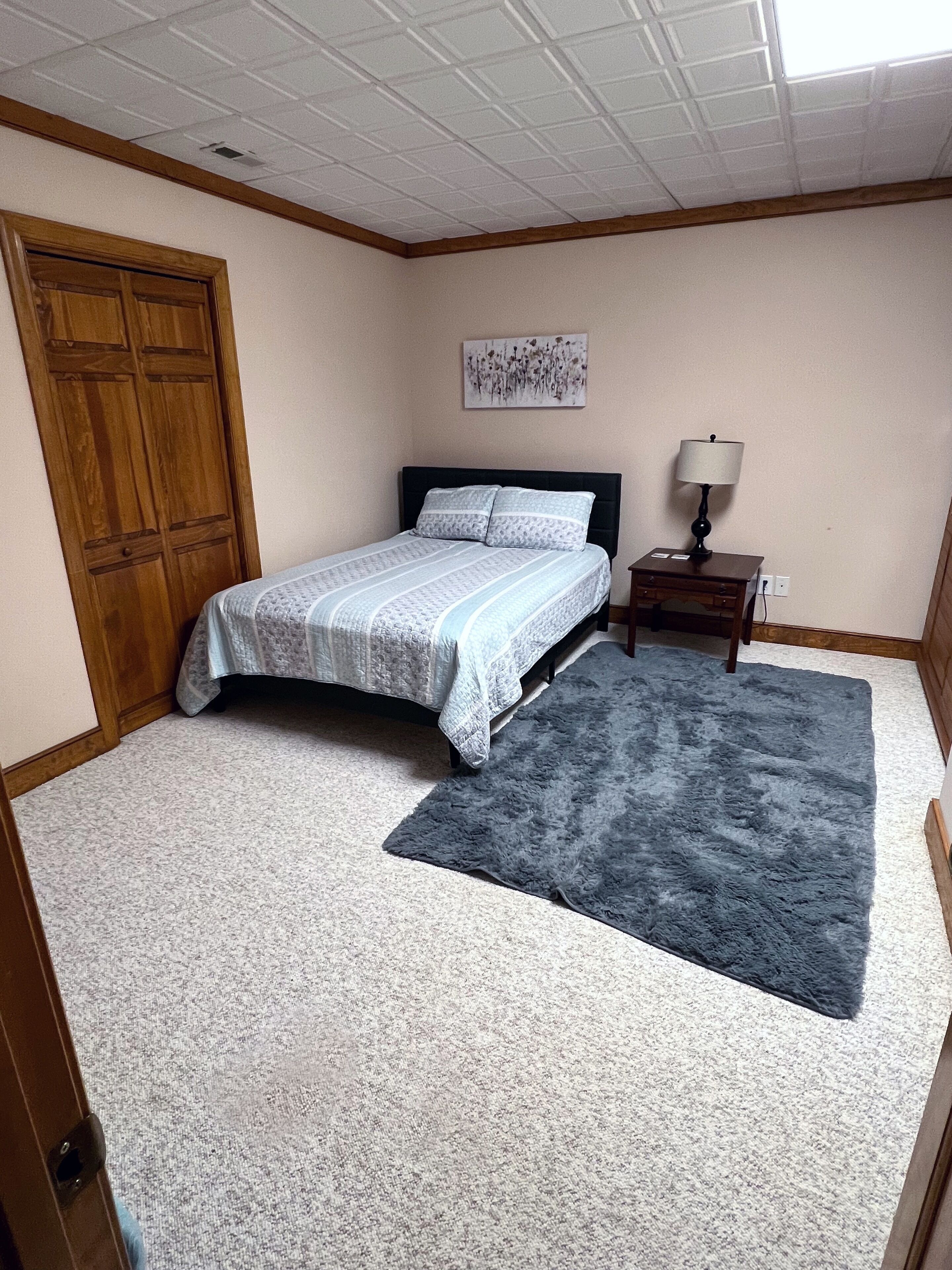 Une chambre à coucher avec un lit, une table de chevet, une lampe, un tapis et une porte.