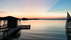 Een rustig meer bij zonsondergang met een steiger en een zeilboot.