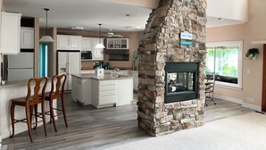 Een moderne keuken met witte kasten, een stenen open haard en een eethoek met houten stoelen.