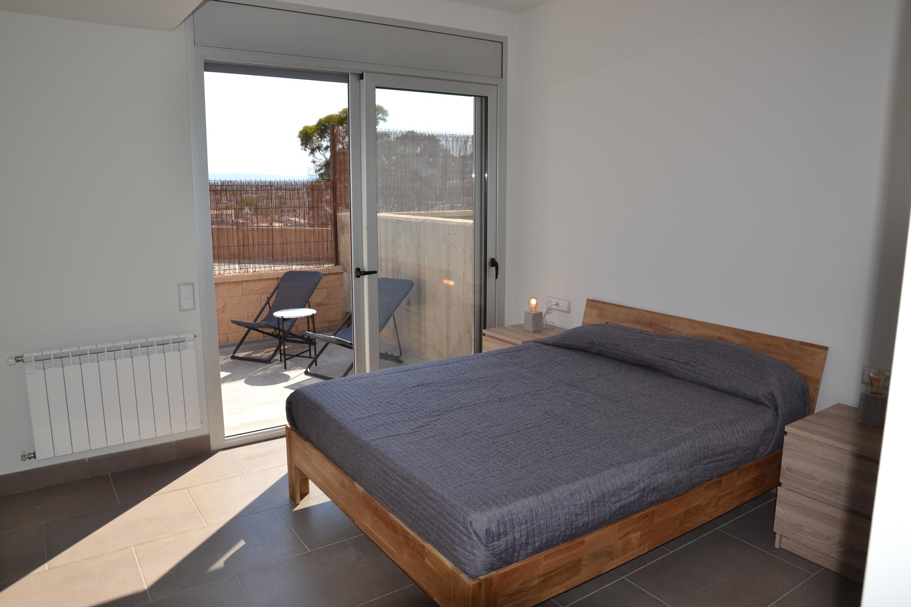 A bedroom with a wooden bed, a sliding glass door leading to an outdoor area with a chair and a table.