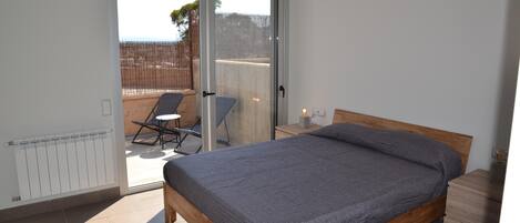 A bedroom with a wooden bed, a sliding glass door leading to an outdoor area with a chair and a table.