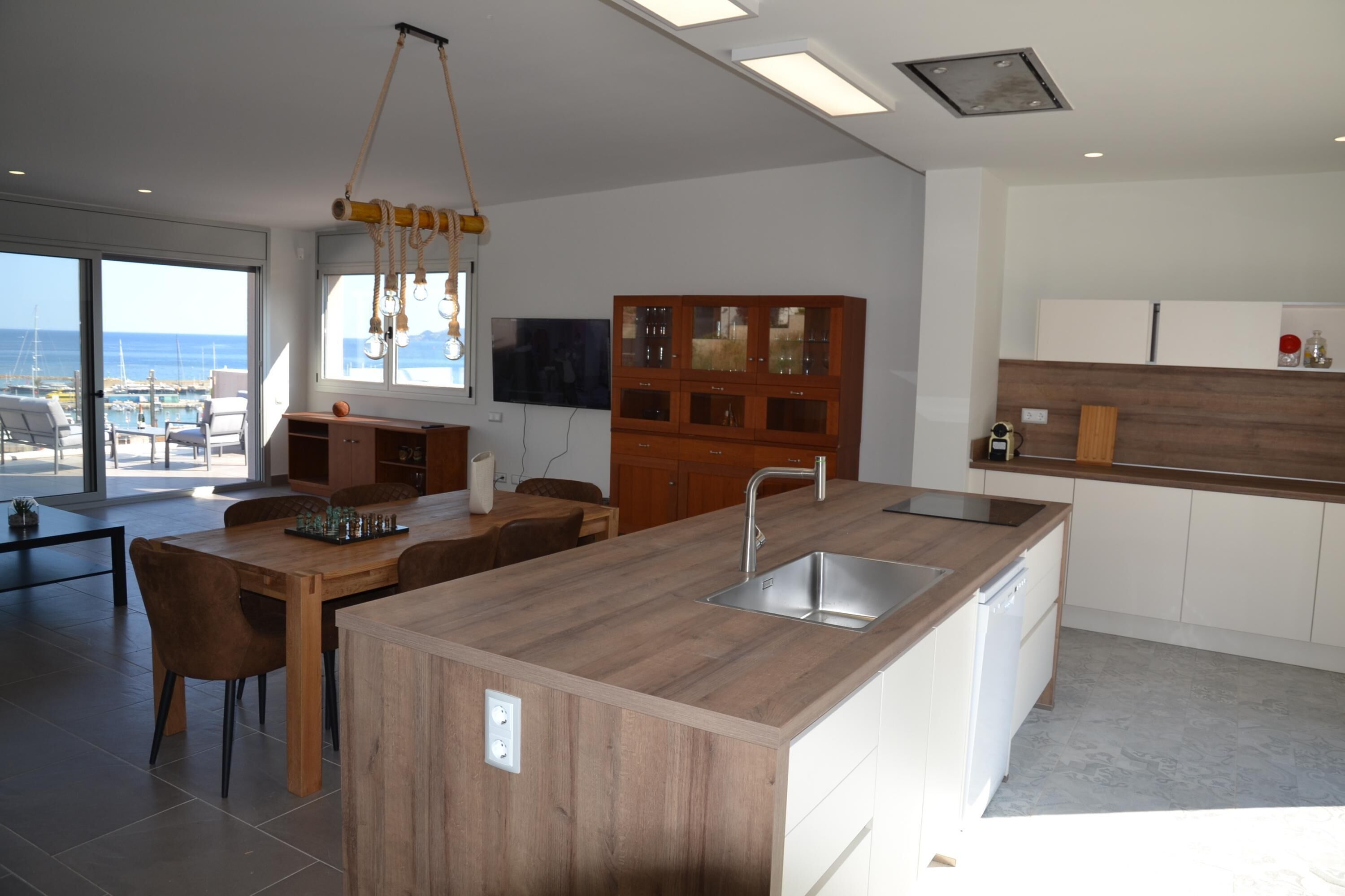 Une cuisine moderne dotée d’un îlot central, de meubles en bois et d’une grande fenêtre donnant sur la mer.