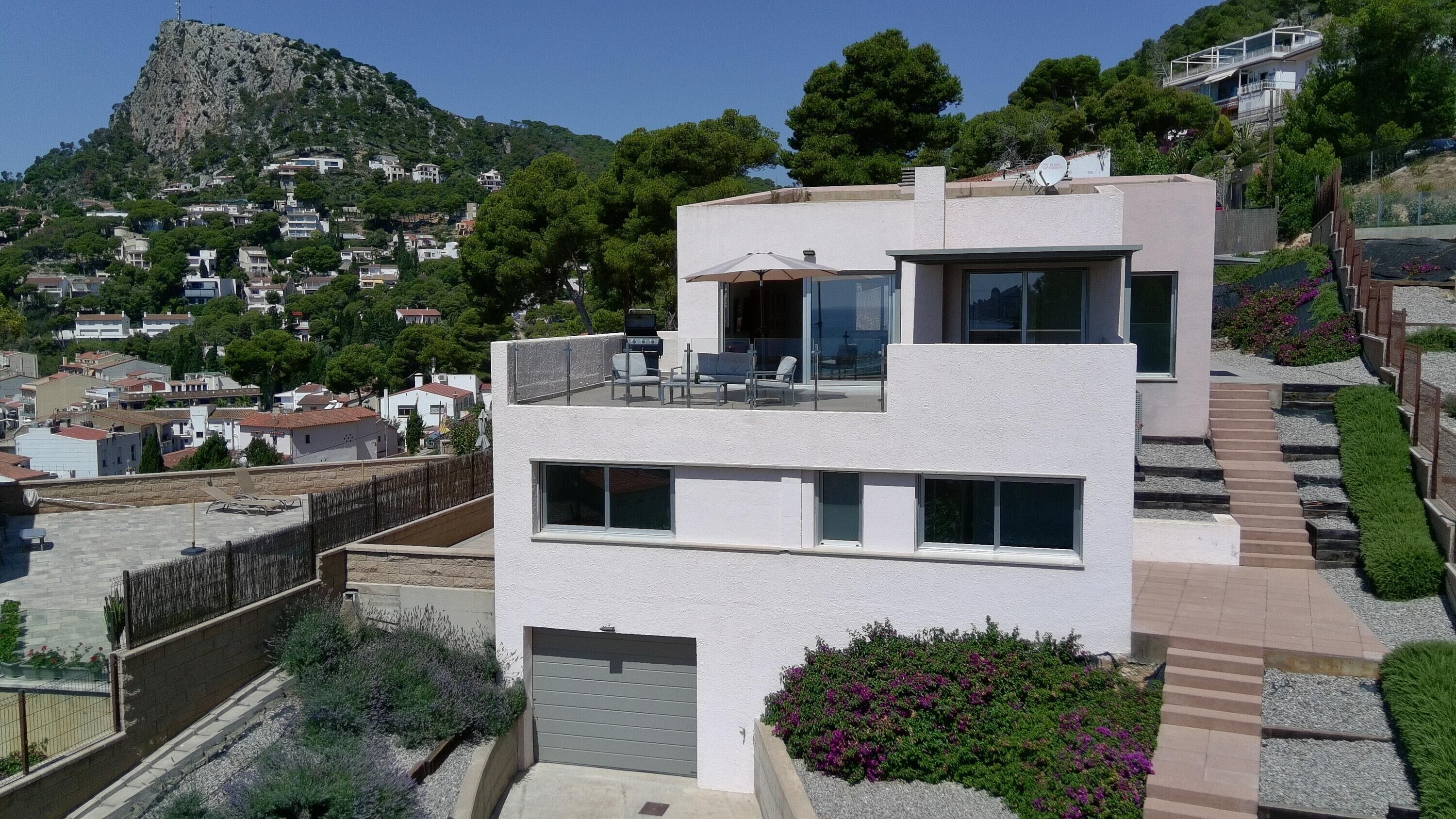 A modern two-story building with a balcony, a garage, and a view of a hillside town.