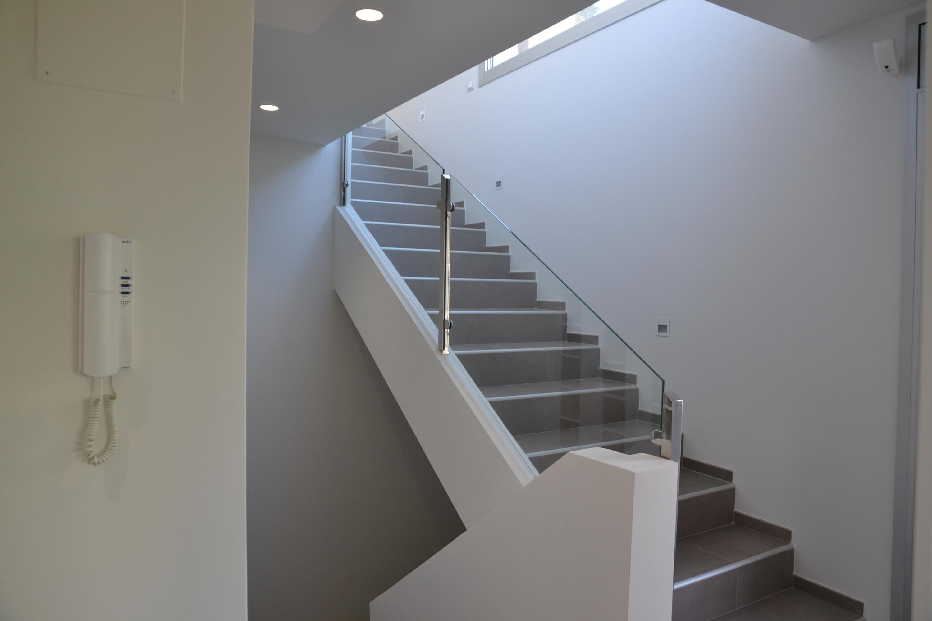 A modern staircase with glass railings and a white wall-mounted telephone.