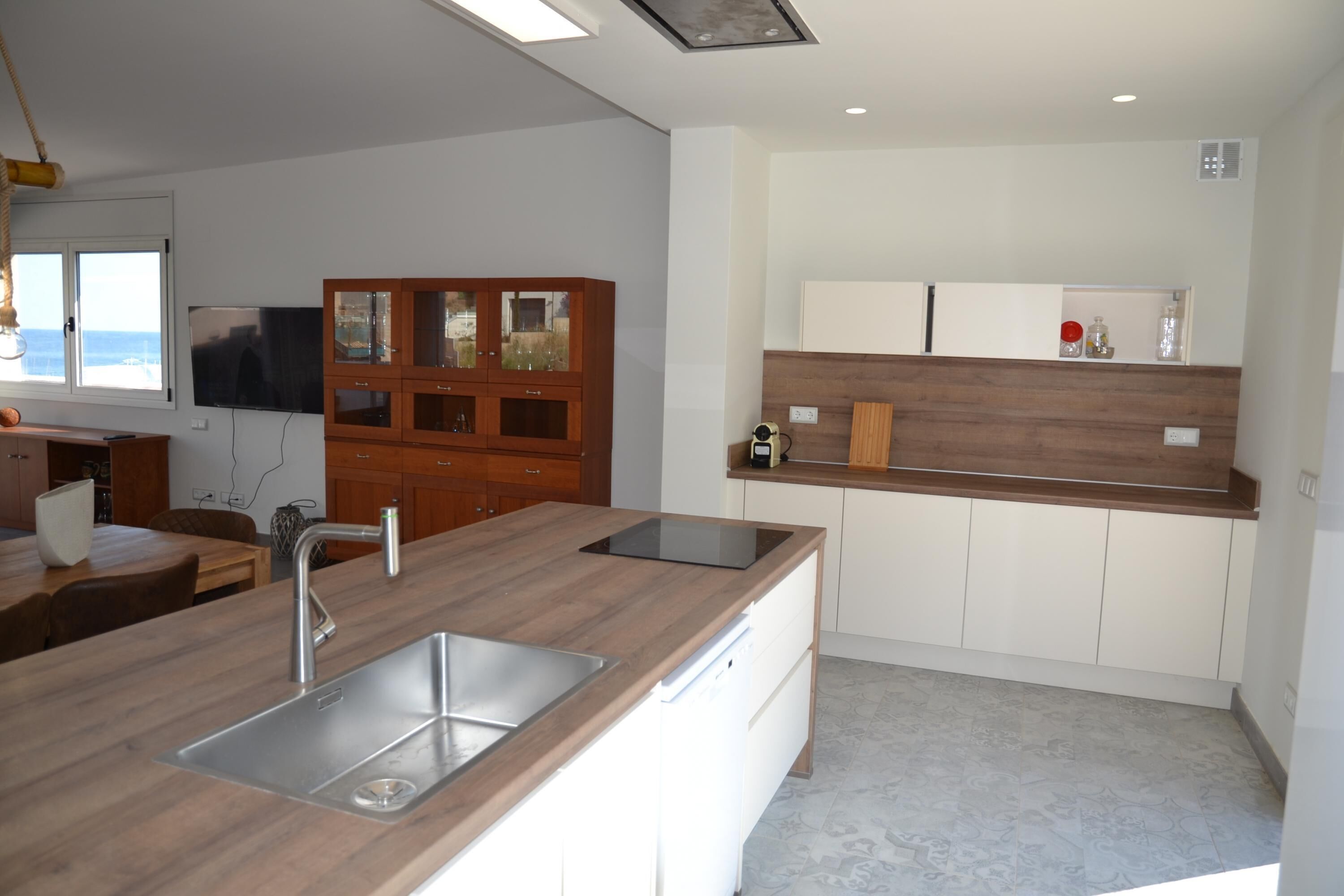 A modern kitchen with a wooden countertop, stainless steel sink, and white cabinets.
