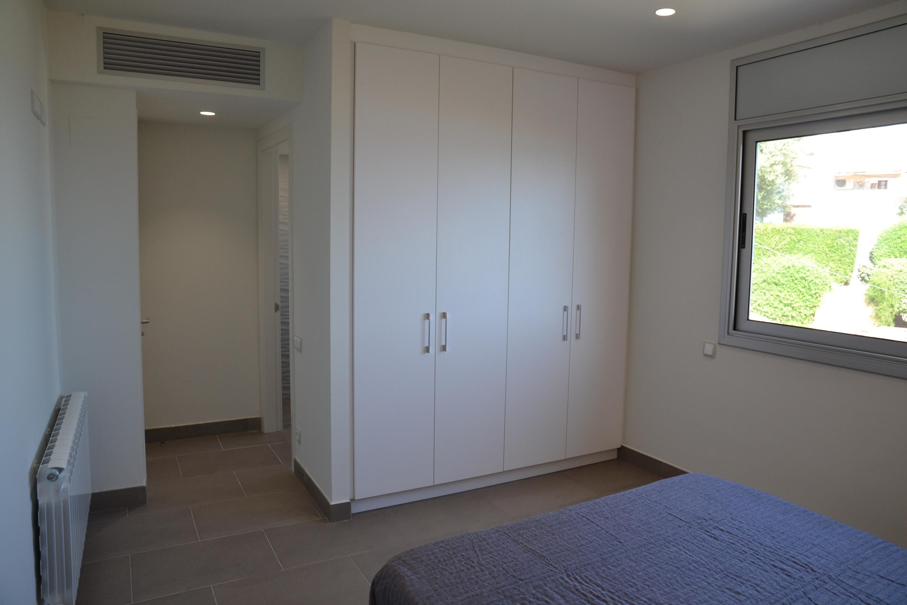 Une chambre à coucher comprenant un lit, une armoire, un radiateur et une fenêtre donnant sur un espace verdoyant.