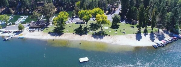 Vue aĂ©rienne dâune propriĂ©tĂ© au bord du lac, avec une plage, des bateaux et un espace de stationnement.
