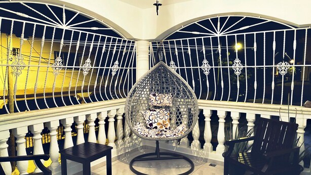 A balcony with a wrought iron railing, a round wicker chair with patterned cushions, and a small table. - Your home away from home! (Cafemba)