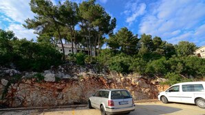 A parking area with a white van and a silver car, surrounded by a rocky hillside and dense trees. - Modern apartment on the beautiful Croatia coast (Prižba)