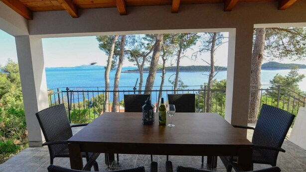 A covered outdoor dining area with a table and chairs, overlooking a scenic view of a lake and trees. - Modern apartment on the beautiful Croatia coast (Prižba)