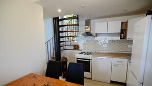 A compact kitchen with white cabinets, a stove, and a dishwasher. There's a wooden dining table with a potted plant. - Modern apartment on the beautiful Croatia coast (Prižba)