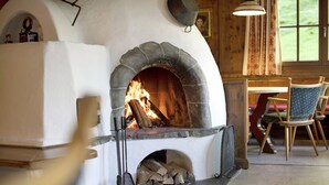 Una chimenea de piedra con fuego, un interior rústico de madera y una zona de comedor con sillas.