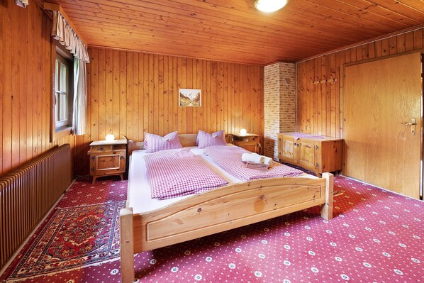 A wooden-paneled room with a bed, a nightstand, a dresser, and a radiator.
