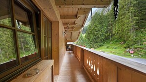 A wooden corridor with large windows, a wooden bench, and a view of a forested mountain area. - Alpine Chalet Lacknerbrunn up to 21 persons with Mountain View (Mayrhofen)