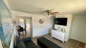 A living room with a black sectional sofa, a white cabinet, a ceiling fan, and a flat-screen TV. - Joe’s Valley Coastal Cottage Left Fork (Orangeville)
