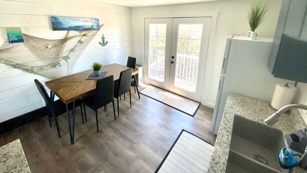 A compact kitchen with a wooden dining table, black chairs, a small potted plant, and a view through the glass doors to the outside. - Joe’s Valley Coastal Cottage Left Fork (Orangeville)
