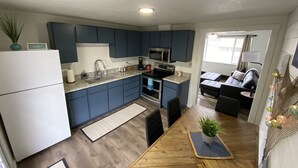 A modern kitchen with dark blue cabinets, a white refrigerator, and a wooden dining table with chairs. - Joe’s Valley Coastal Cottage Left Fork (Orangeville)