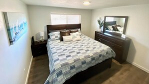 A bedroom with a bed, nightstands, a dresser, a mirror, a window with blinds, and a painting on the wall. - Joe’s Valley Coastal Cottage Left Fork (Orangeville)
