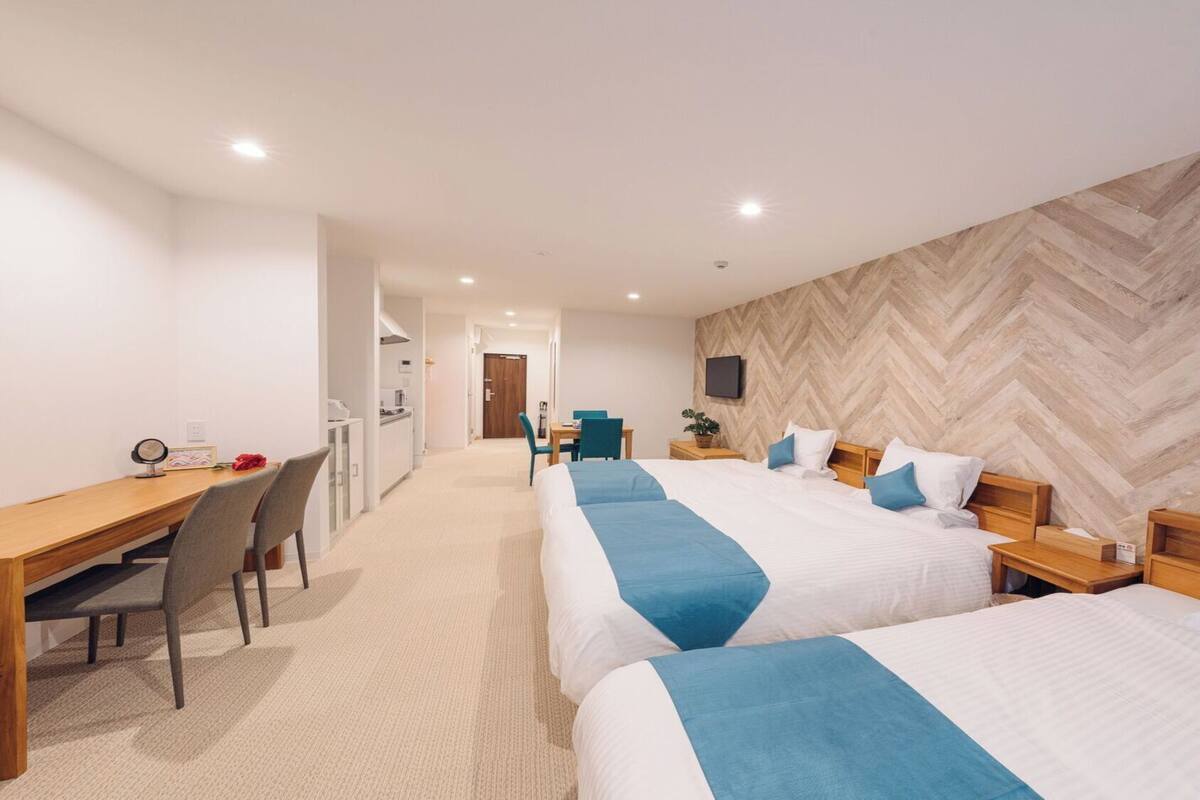 A hotel room with two beds, a desk, a chair, a TV, and a herringbone-patterned wall.